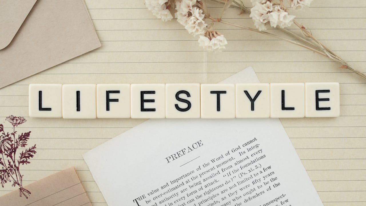 Scrabble tiles spell 'Lifestyle' on lined paper, surrounded by flowers and documents.